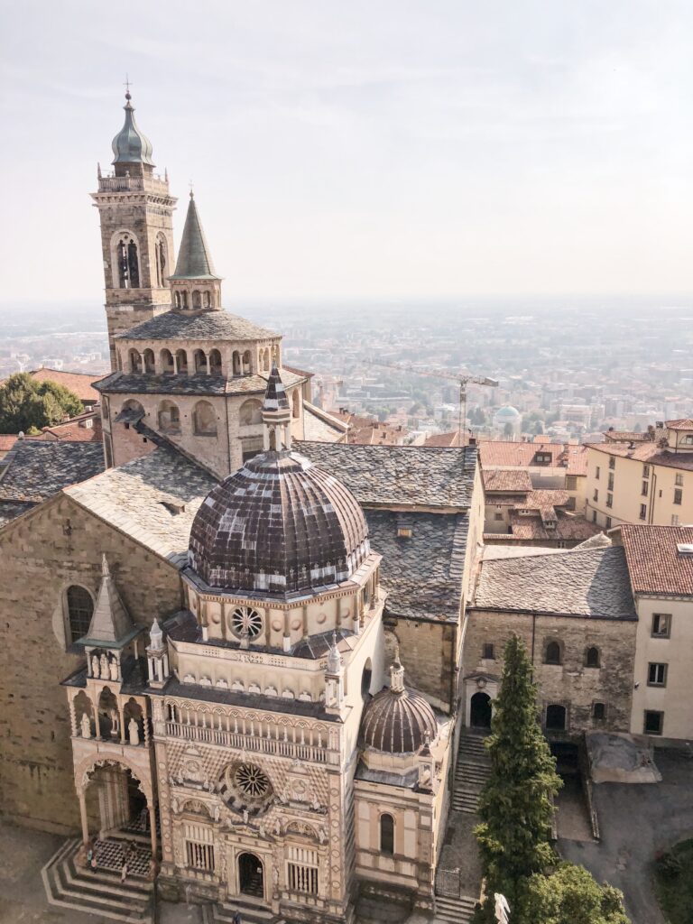 Renaissance facade of Basilica di Santa Maria Maggiore in Bergamo, Italy, with its ornate domes and spires overlooking the modern city below.